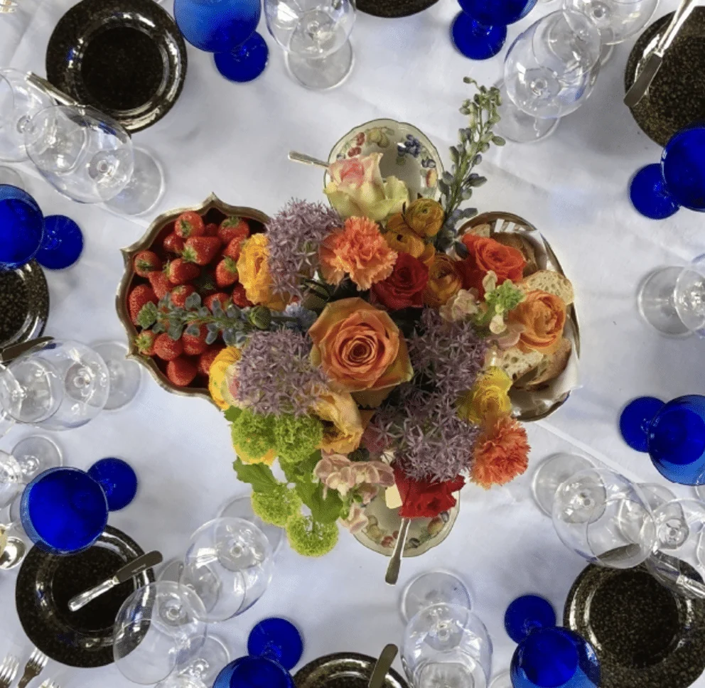 Banquet table seen from above, with a flower arrangement, strawberries and blue glasses